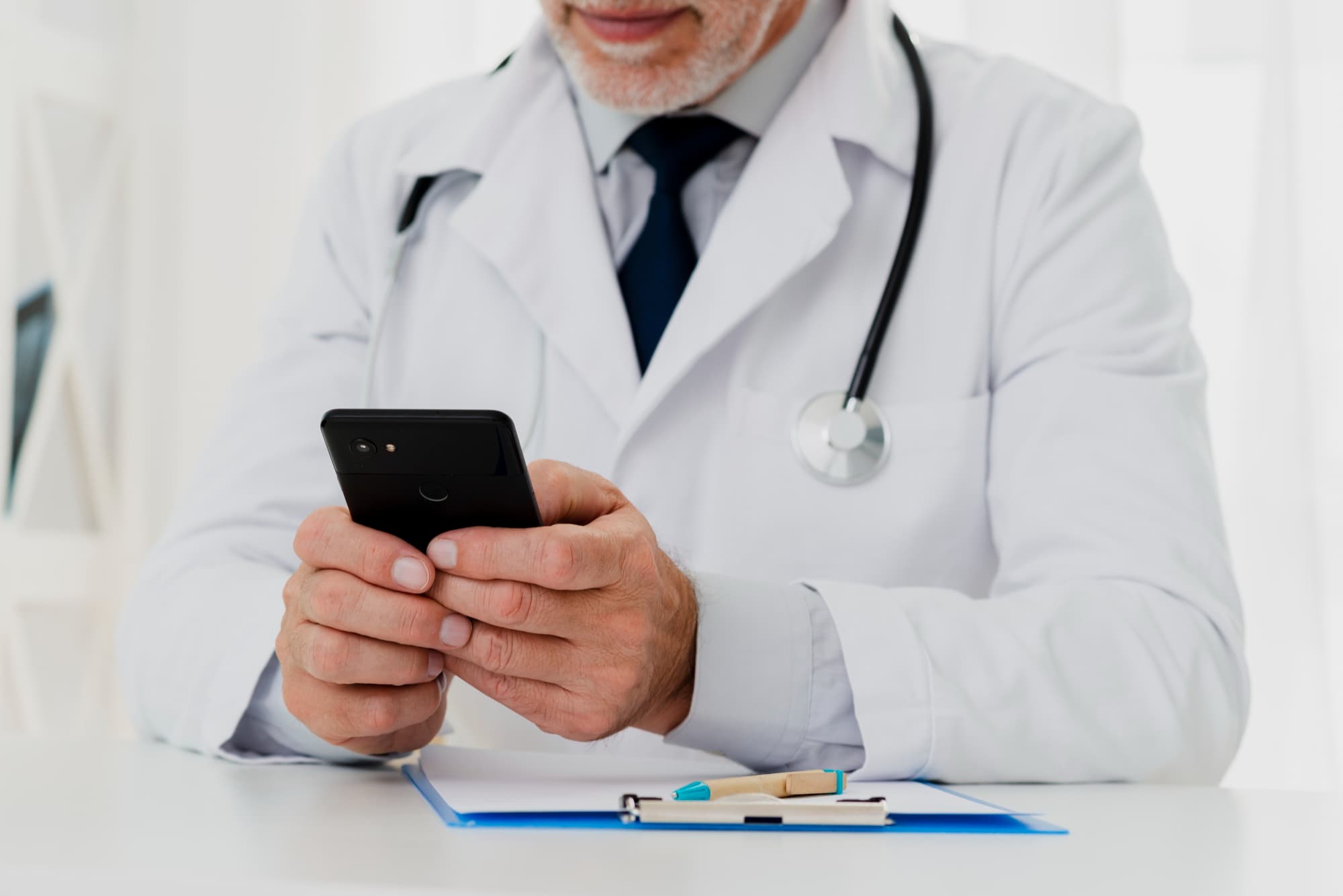 Médico con estetoscopio revisando la consulta desde su teléfono